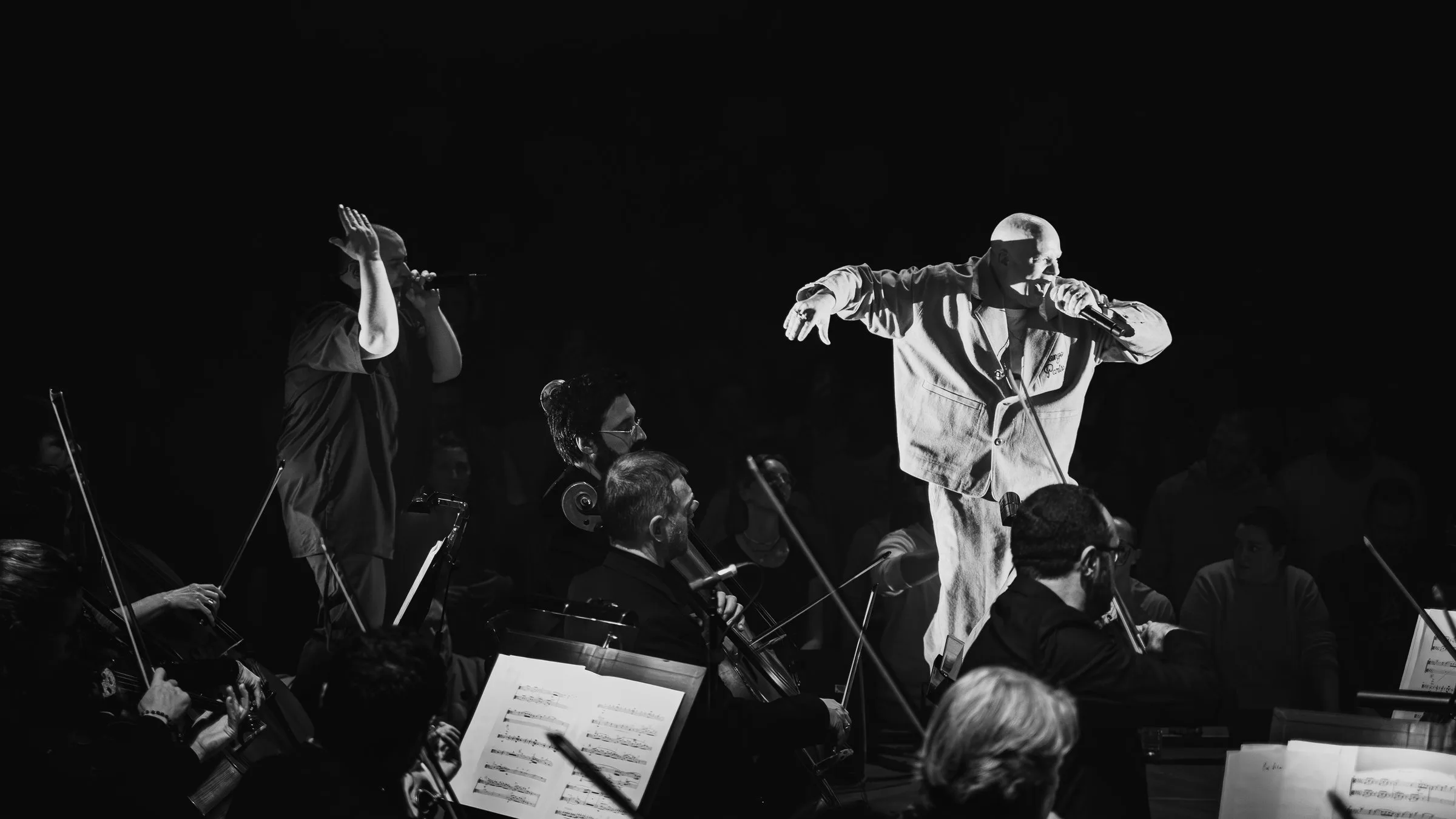 Scylla et un chanteur, bras levés au-dessus de l’orchestre, en noir et blanc