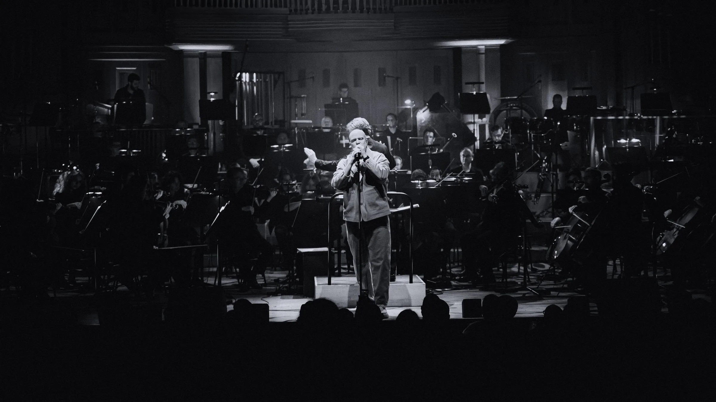 Scylla seul dans la lumière devant l’orchestre, en noir et blanc