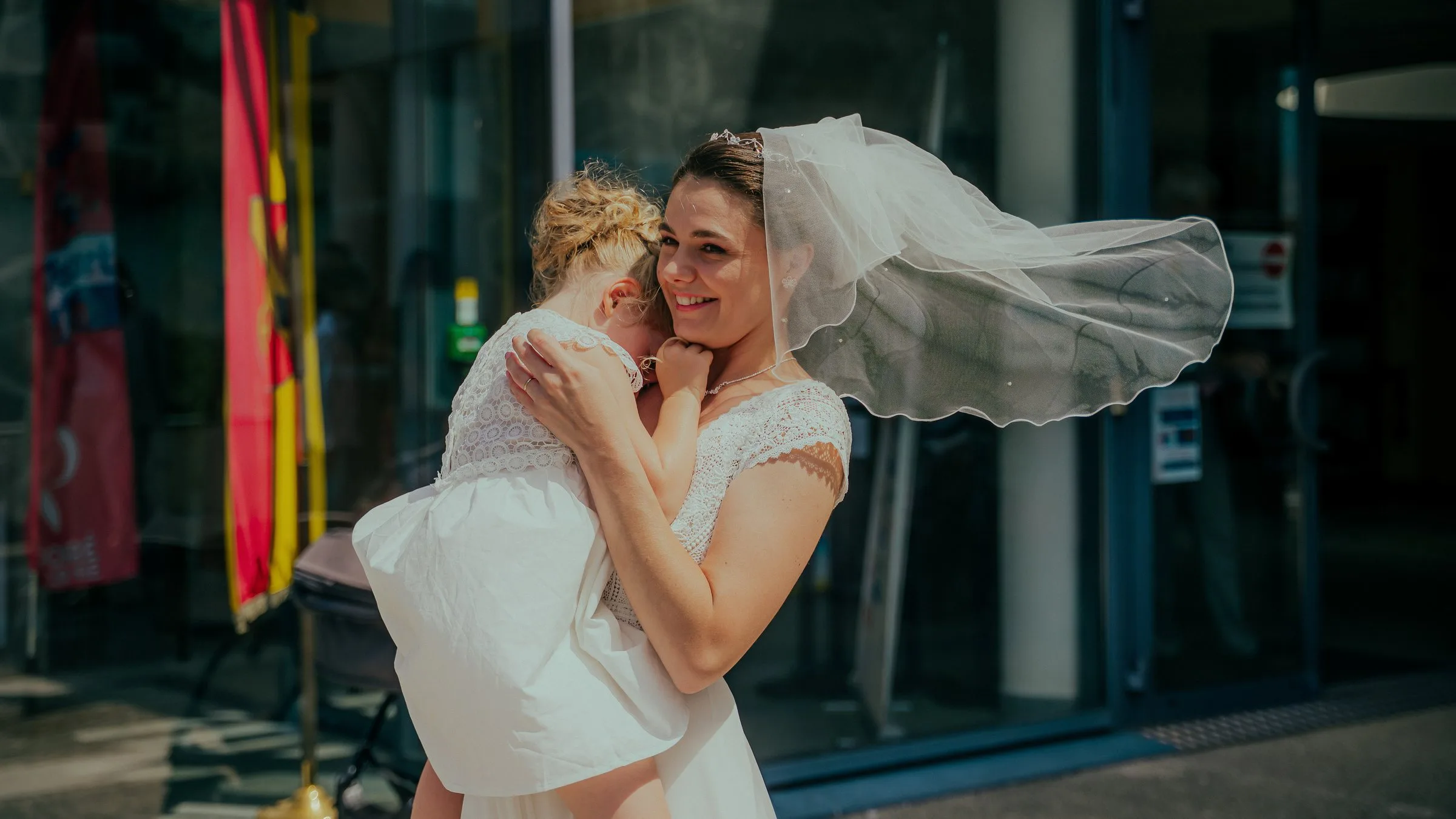 La mariée serre un enfant contre elle, le voile au vent