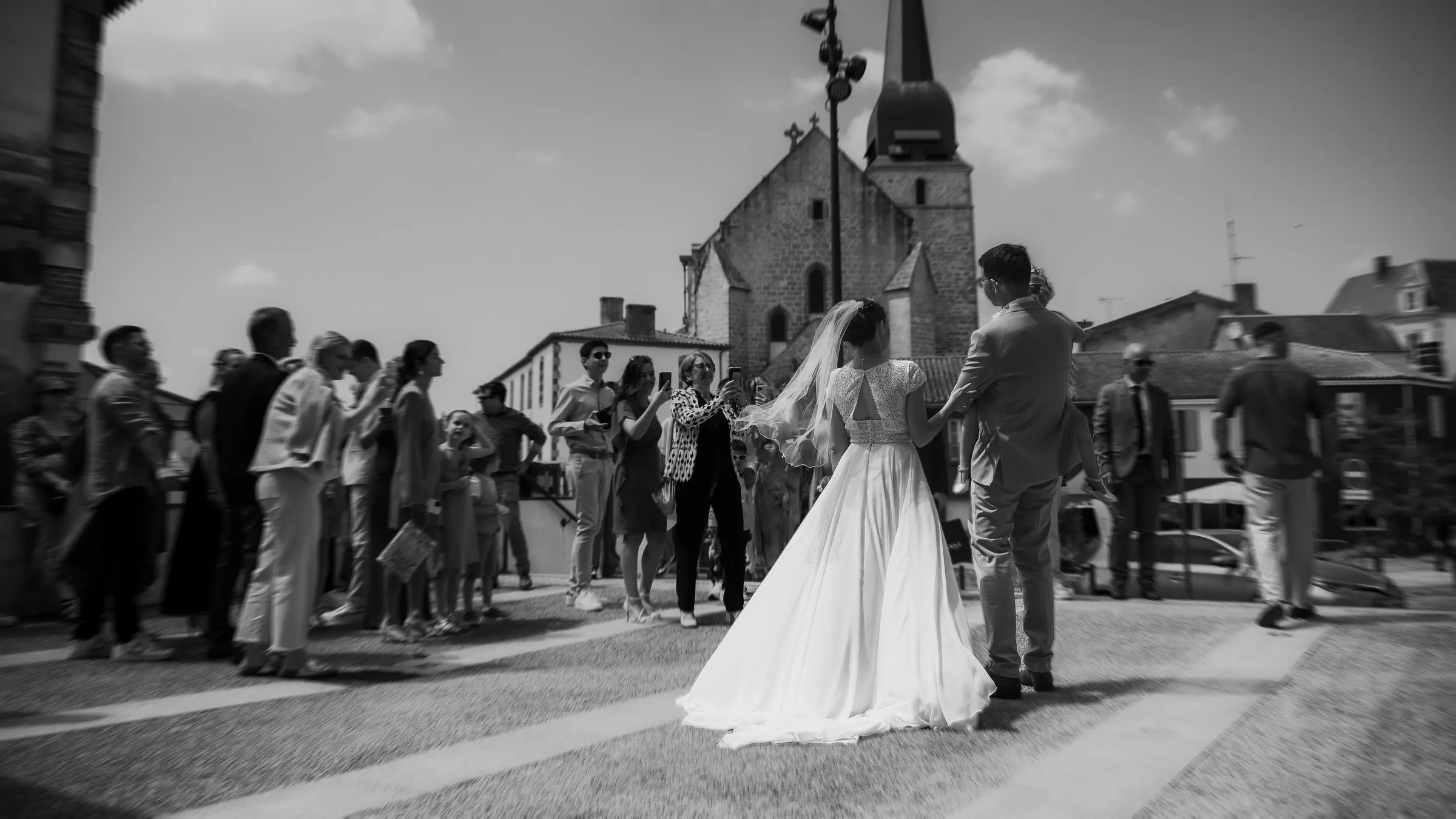 Les mariés sur le parvis de l’église, face à leurs invités, en noir et blanc