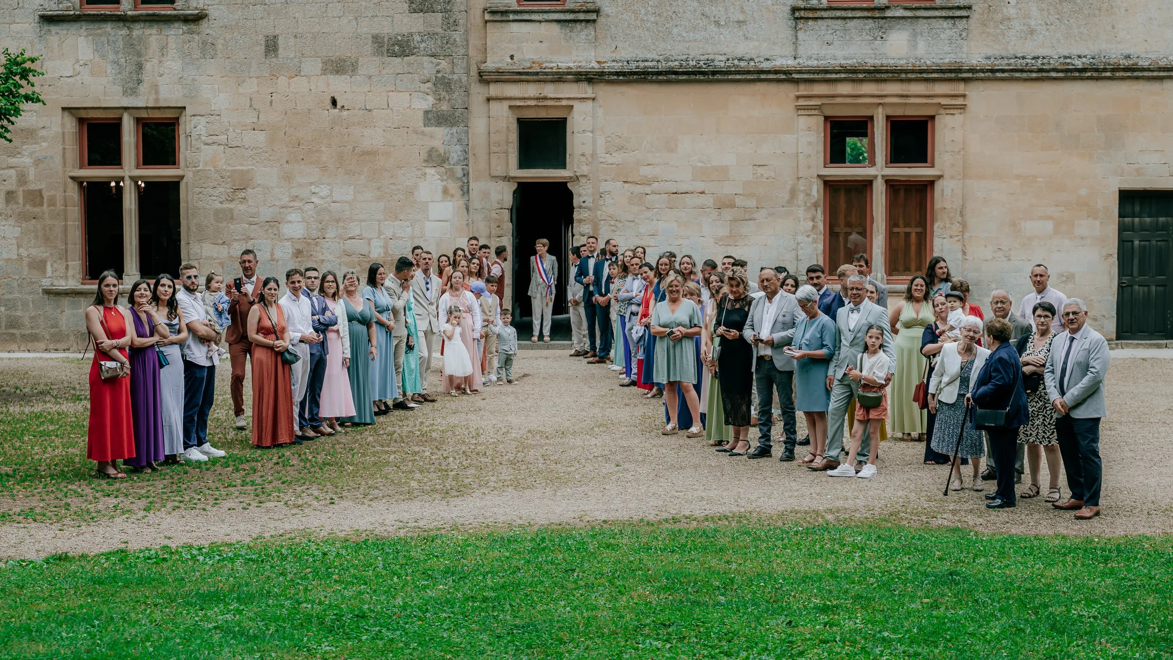 Les invités attendent les mariés devant une façade en pierre