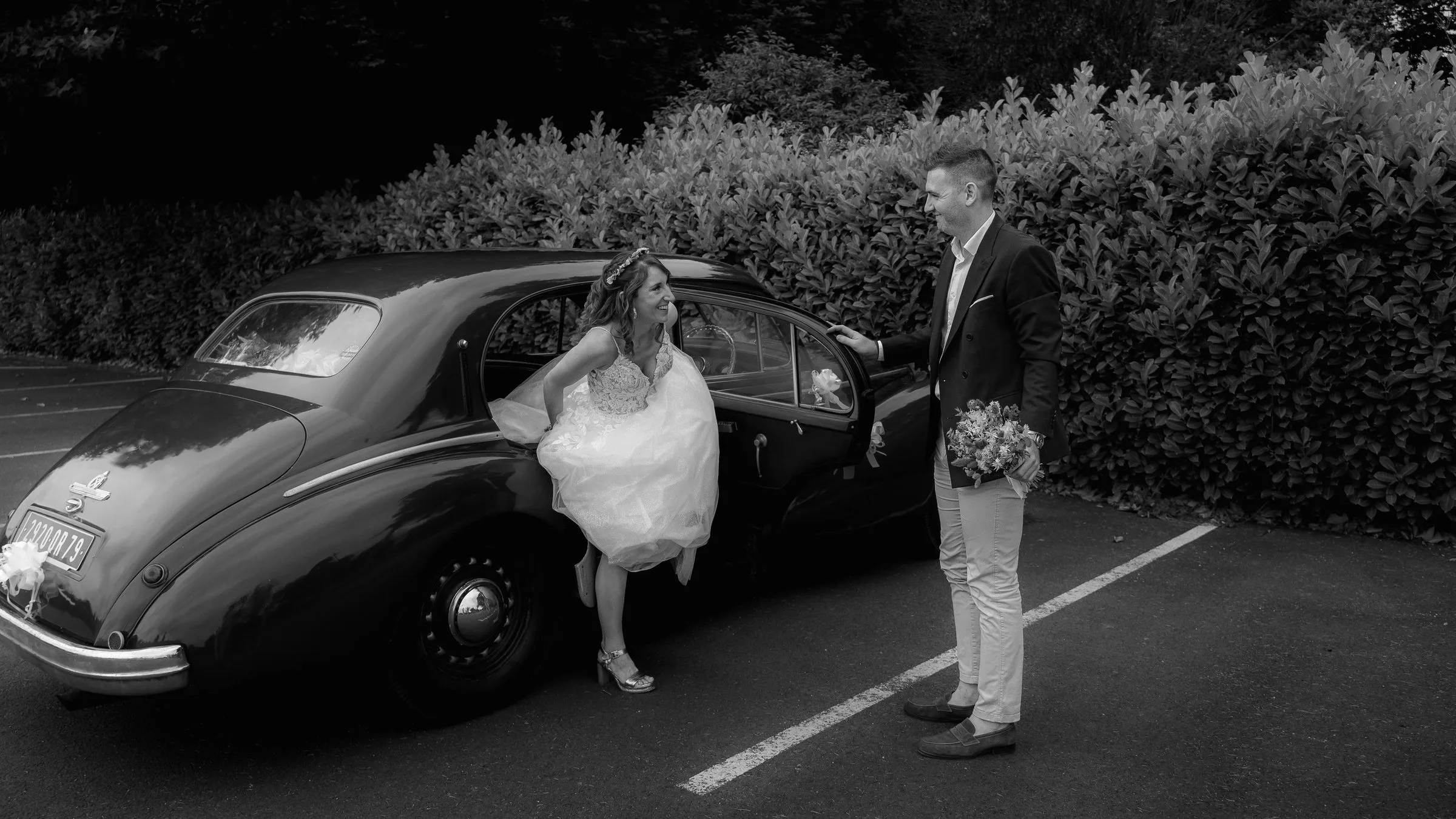 La mariée sort de la voiture ancienne, en noir et blanc