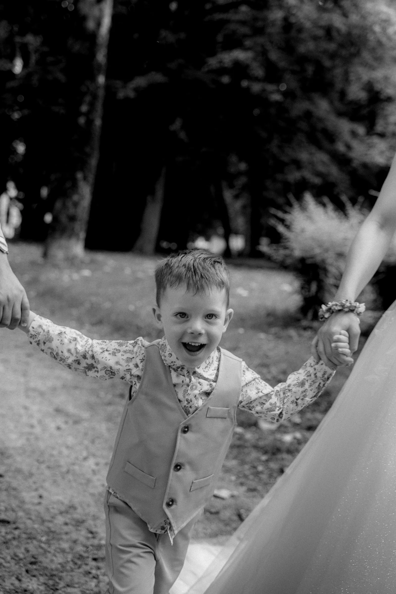 Un petit garçon rit en tenant la main de la mariée, en noir et blanc