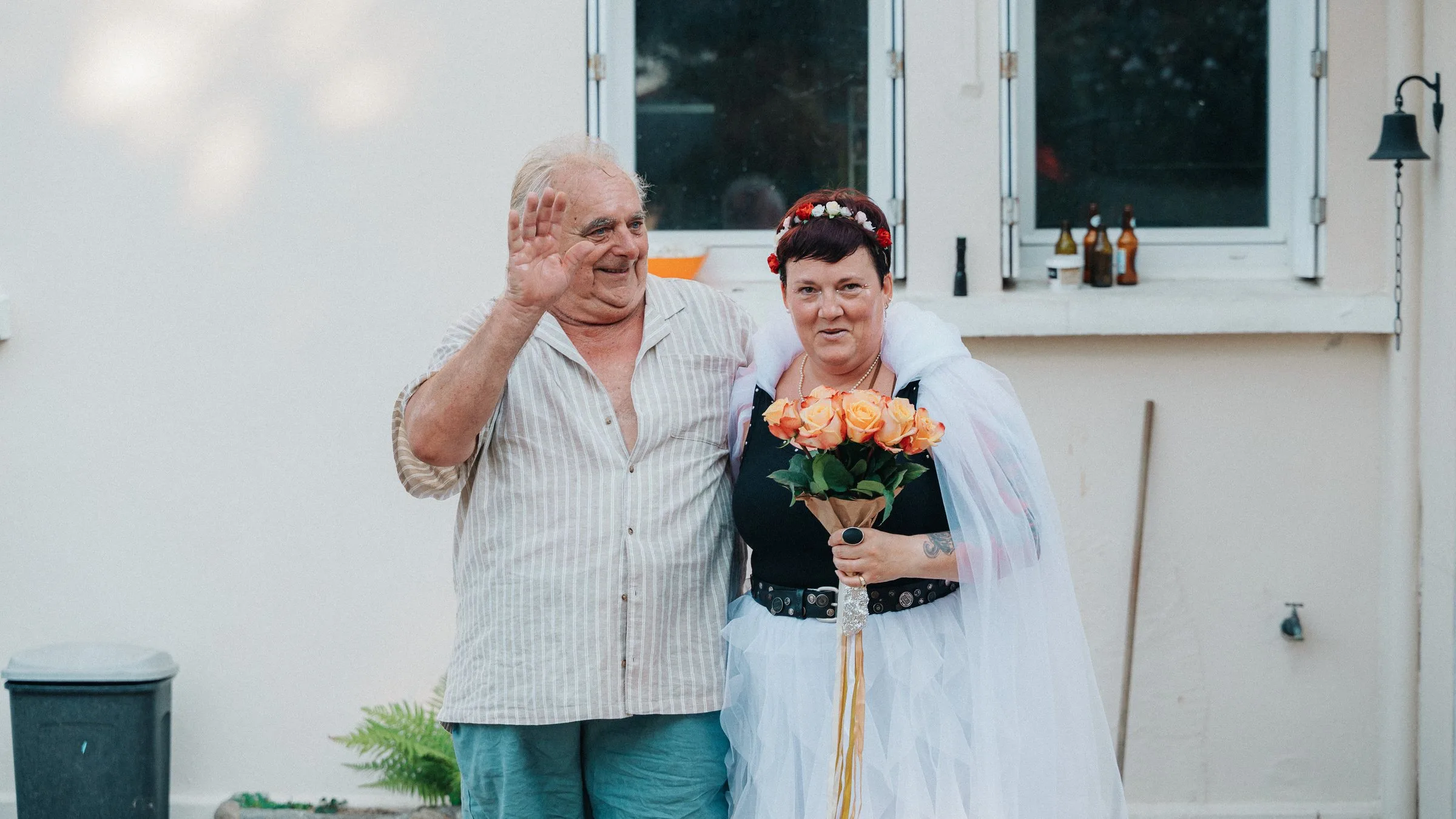 La mariée, bouquet à la main, et un proche saluent les invités