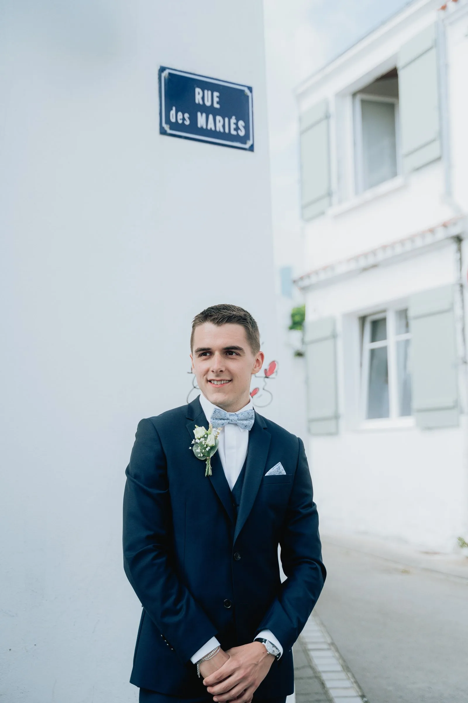 Le marié attend sous la plaque « Rue des Mariés »
