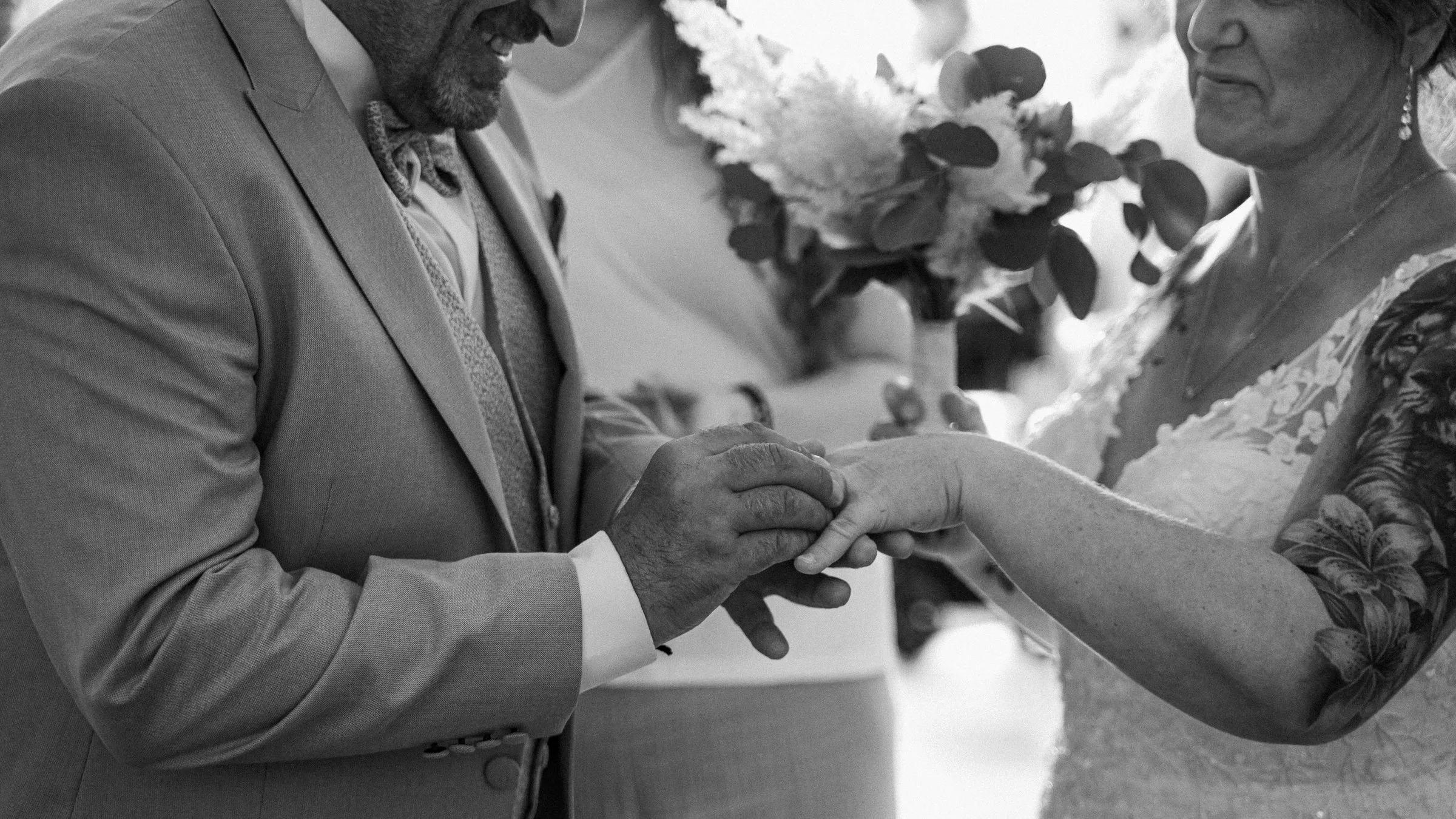 Le marié glisse l’alliance au doigt de la mariée, en noir et blanc