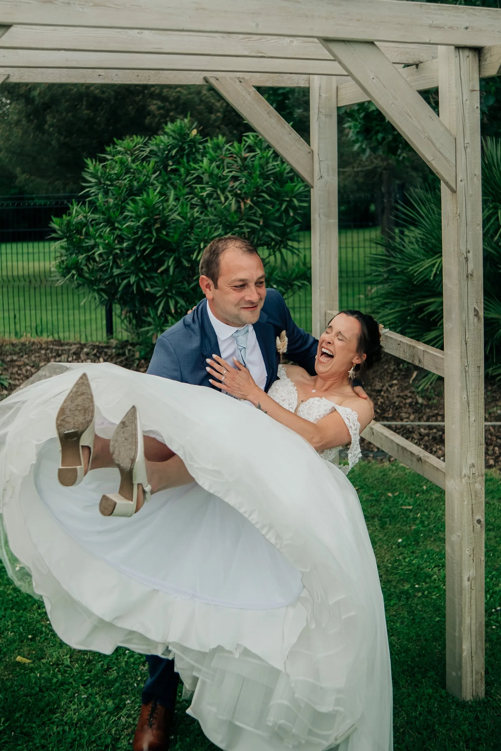 Le marié soulève la mariée en riant sous la pergola