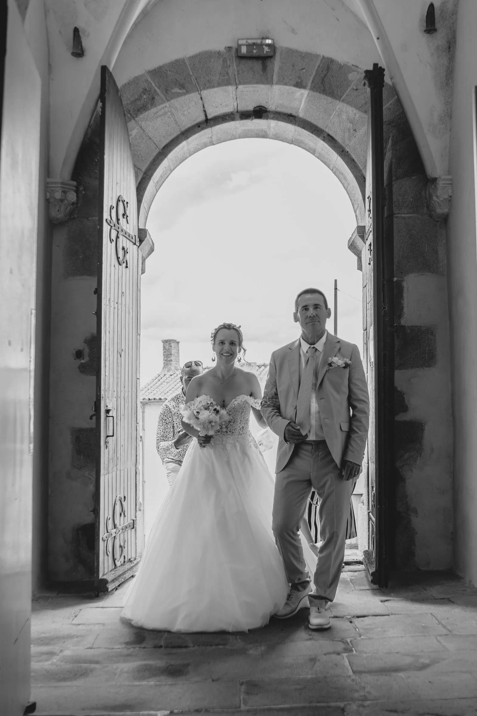 La mariée entre dans l’église au bras d’un proche, en noir et blanc
