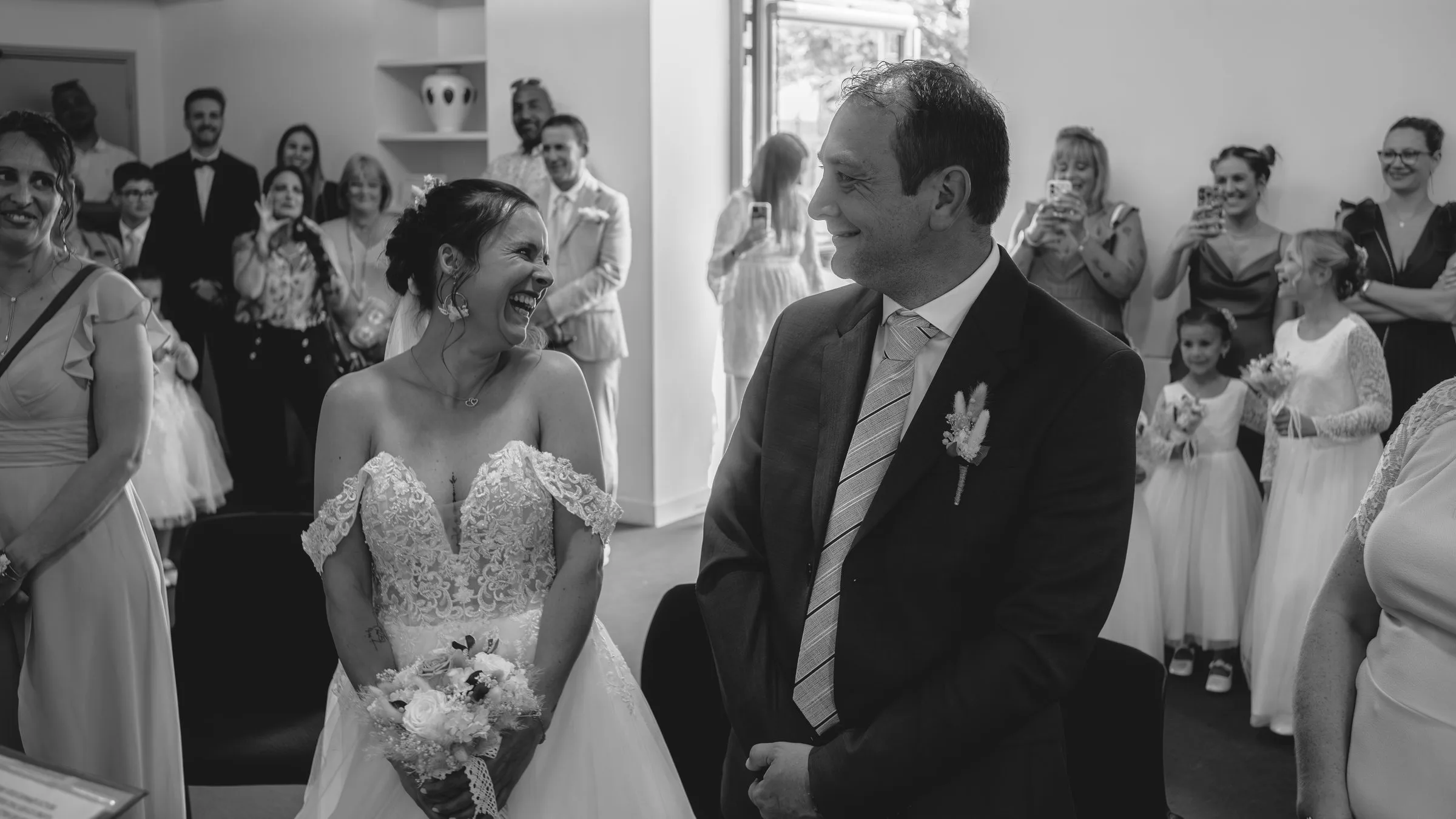 Les mariés rient au milieu de leurs invités, en noir et blanc
