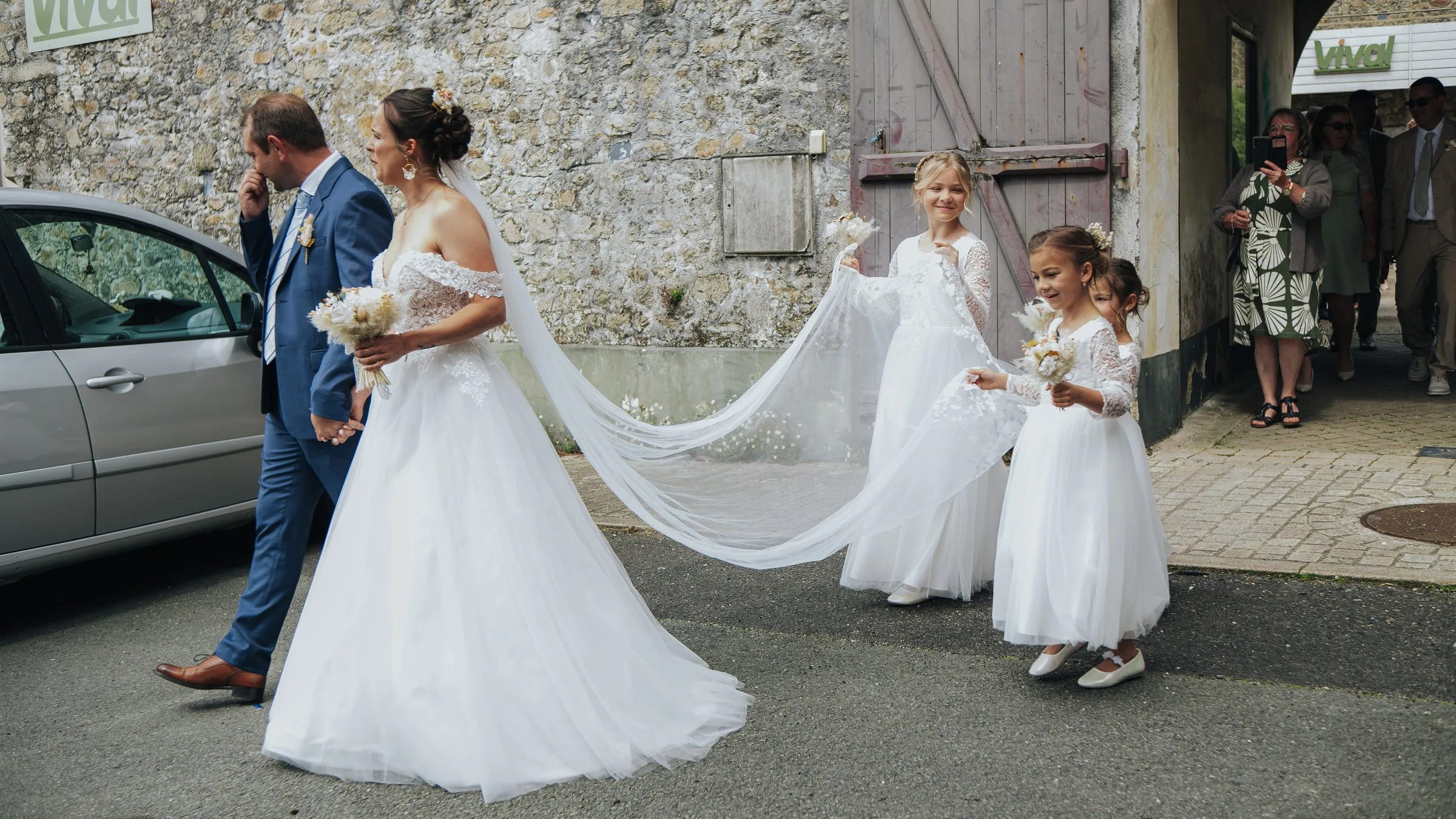 La longue traîne de la mariée portée par les demoiselles d’honneur, en route vers l’église