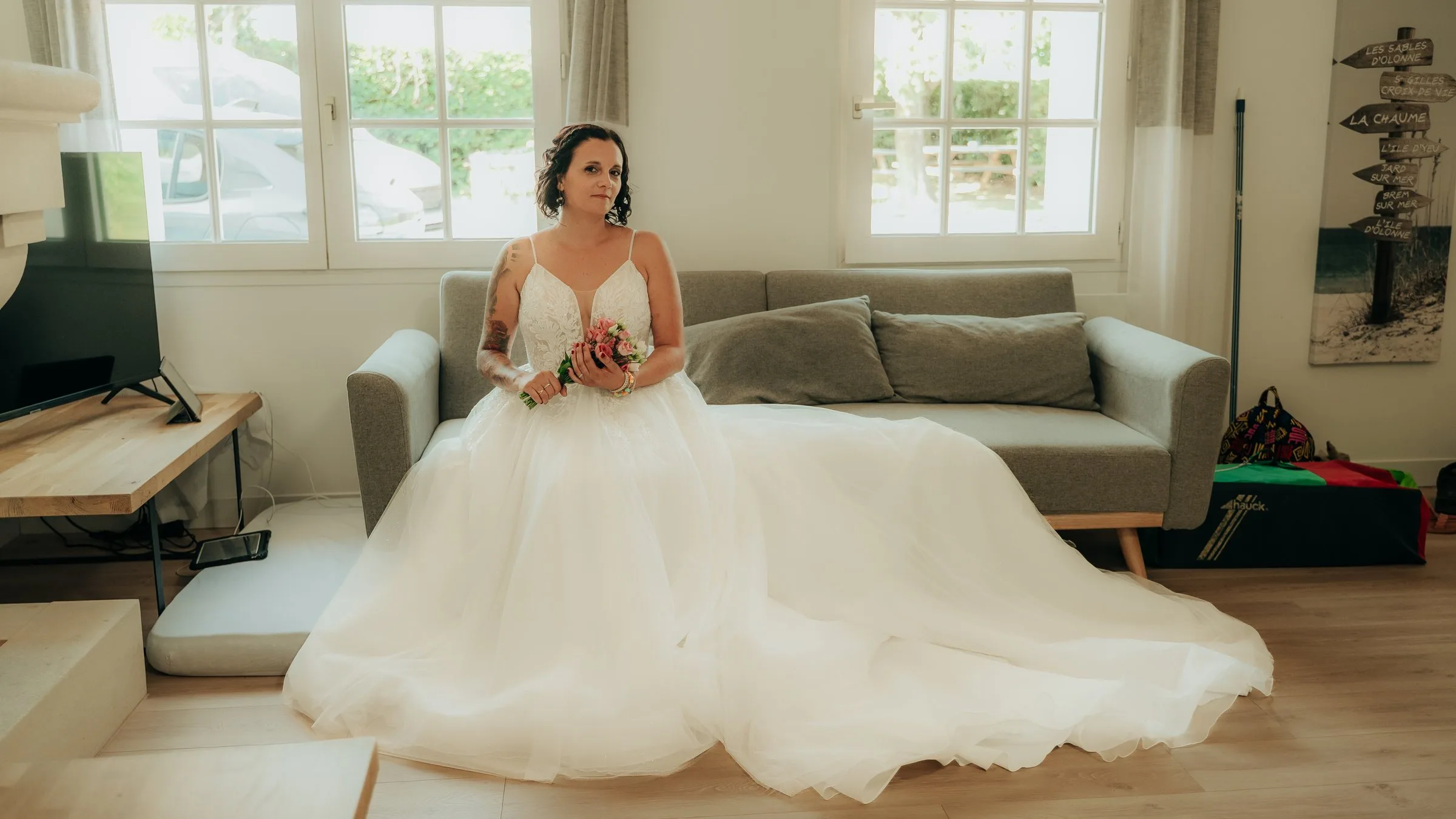 La mariée assise sur le canapé, sa robe étalée autour d’elle
