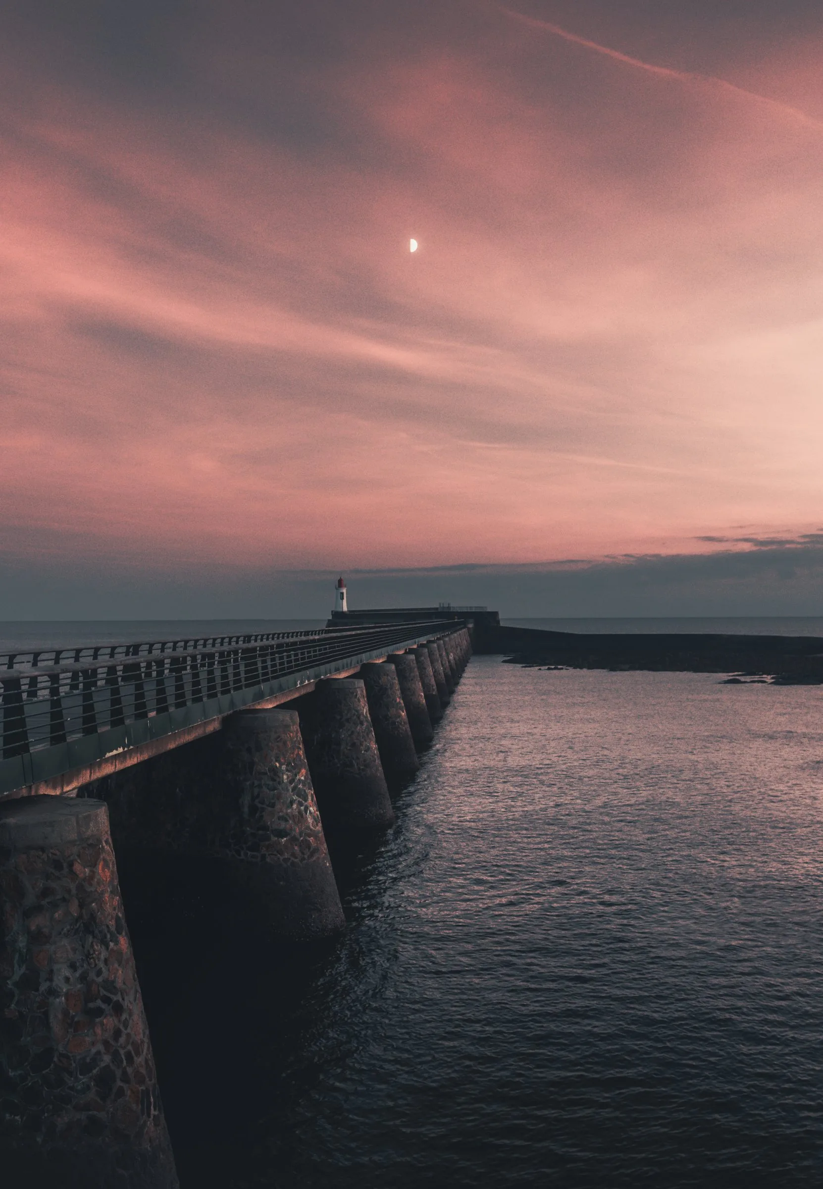 La jetée et son phare sous un ciel rose, la lune au-dessus
