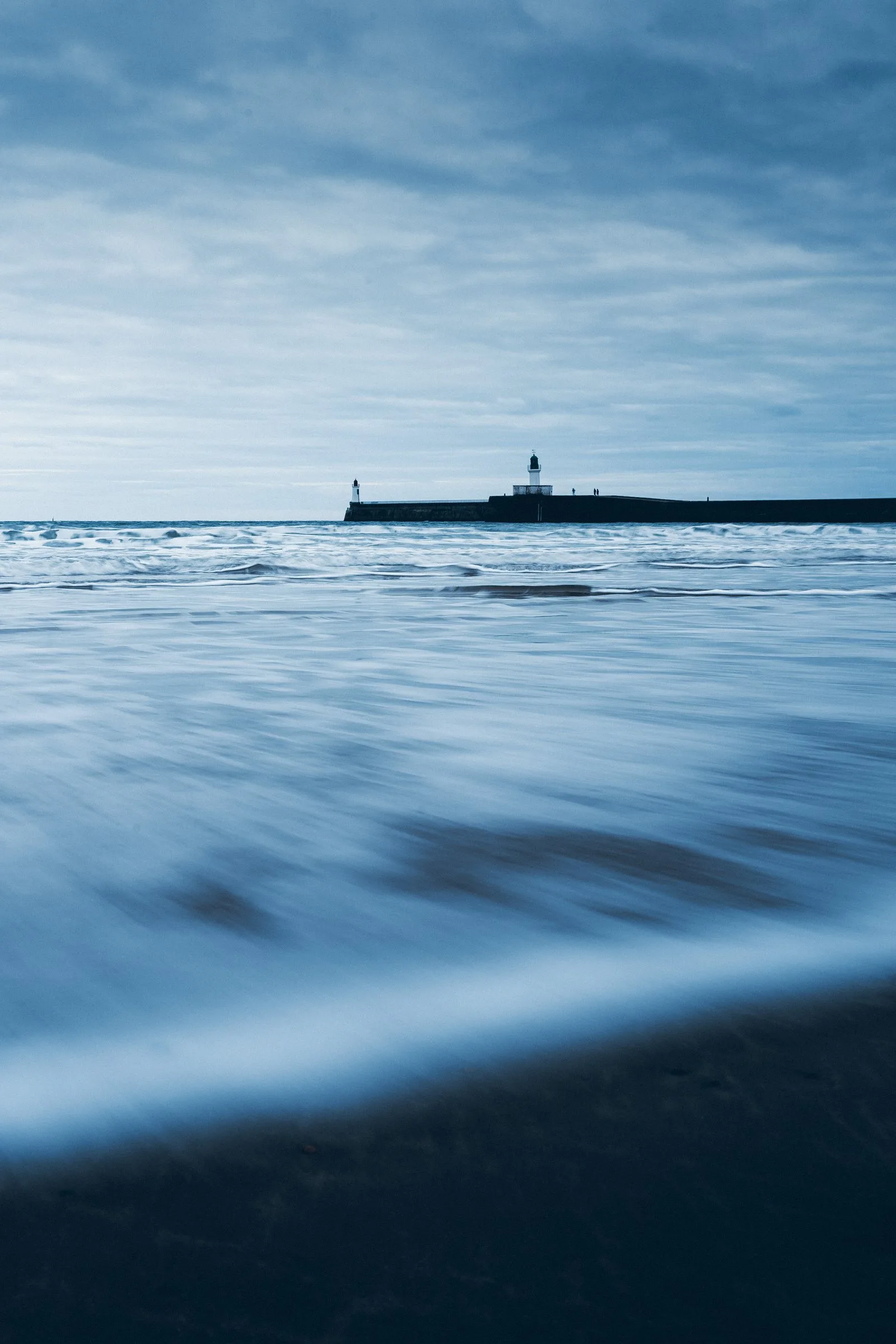 Pose longue sur l’océan, le phare de la jetée à l’horizon