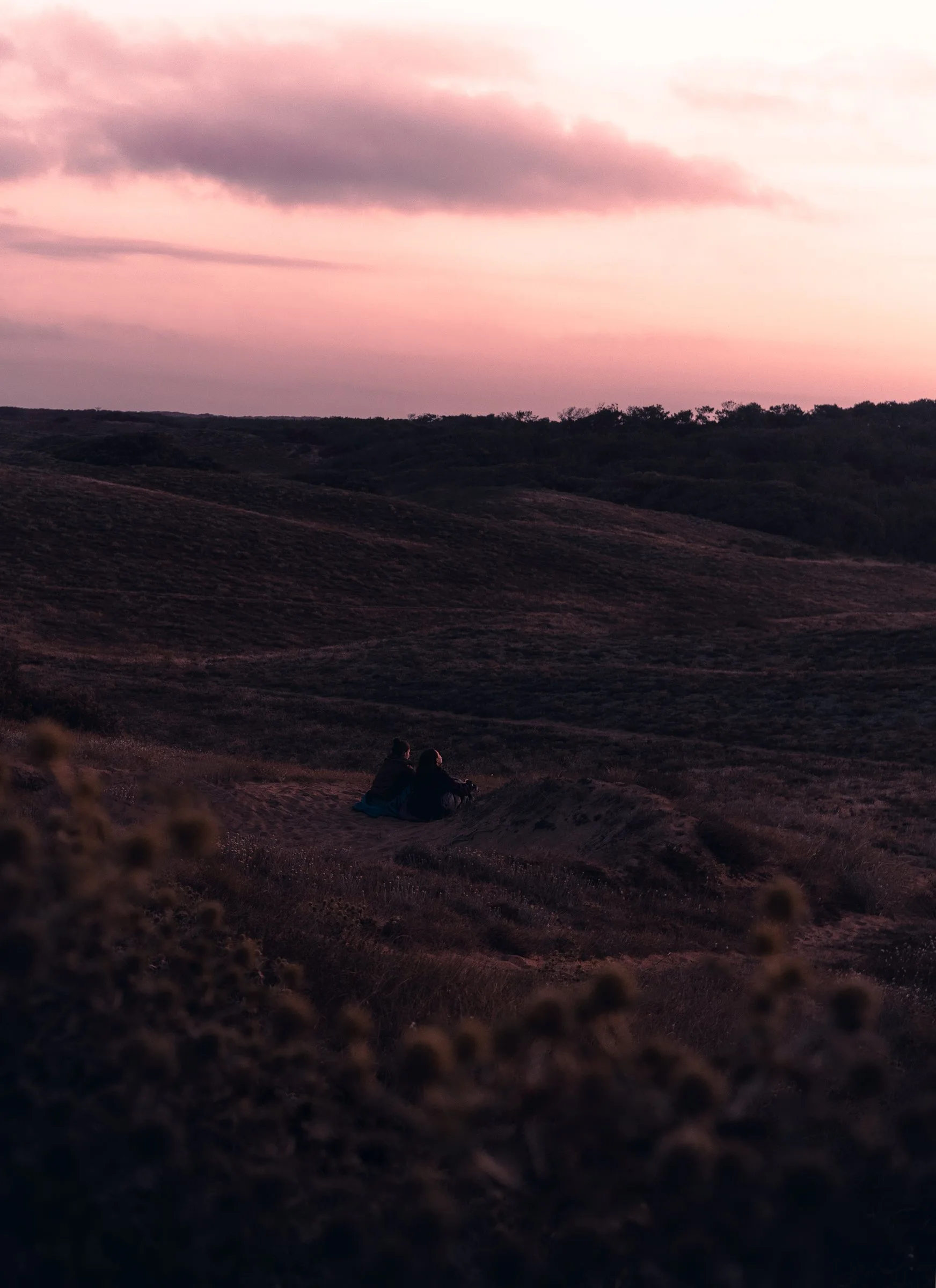 Deux silhouettes dans les dunes sous un ciel rose