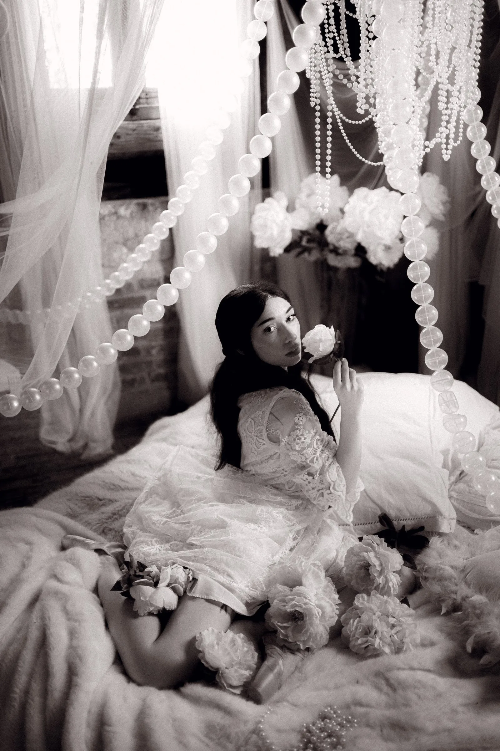Femme allongée parmi les voilages et les perles, en noir et blanc
