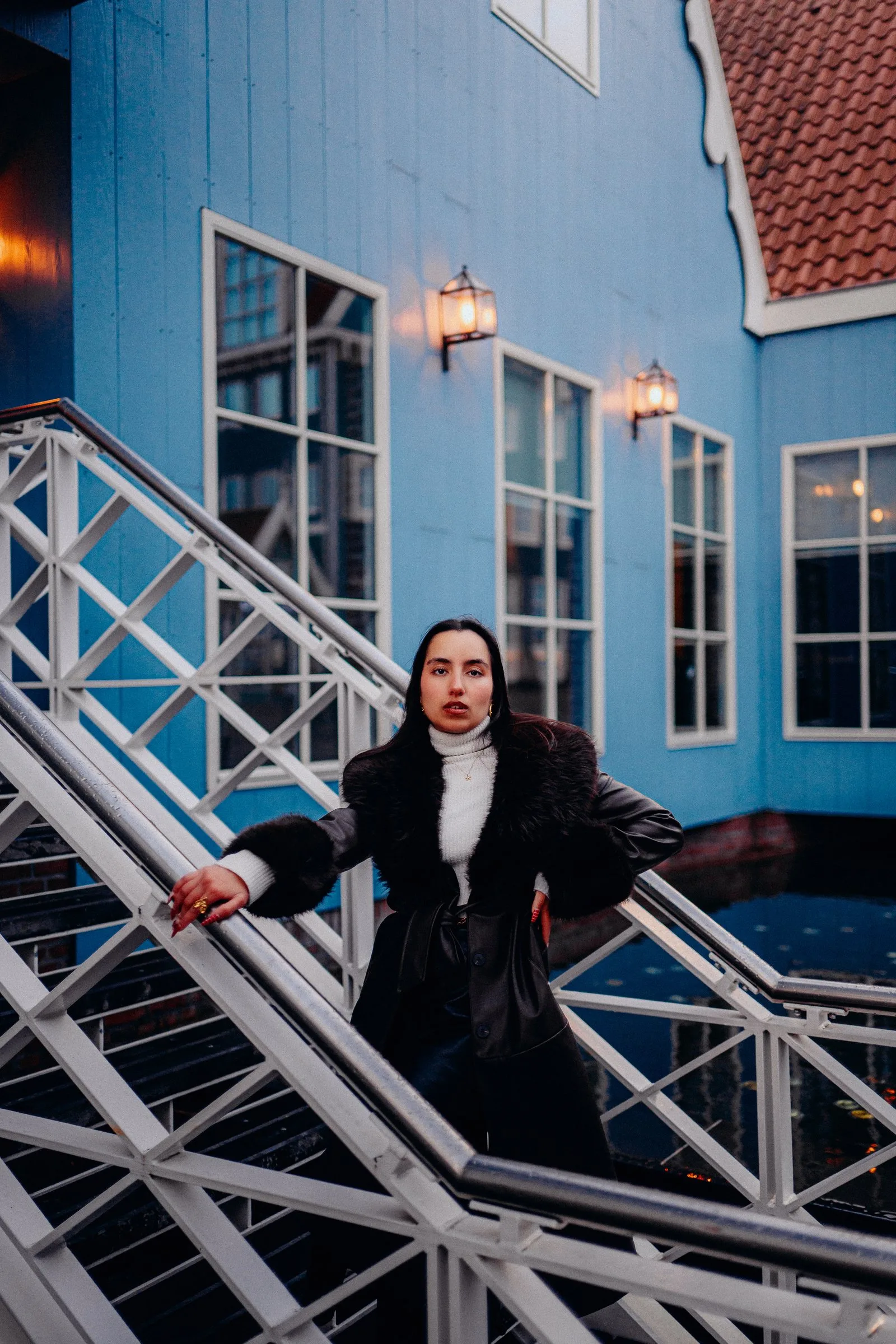 Femme en manteau noir sur un escalier devant une maison bleue