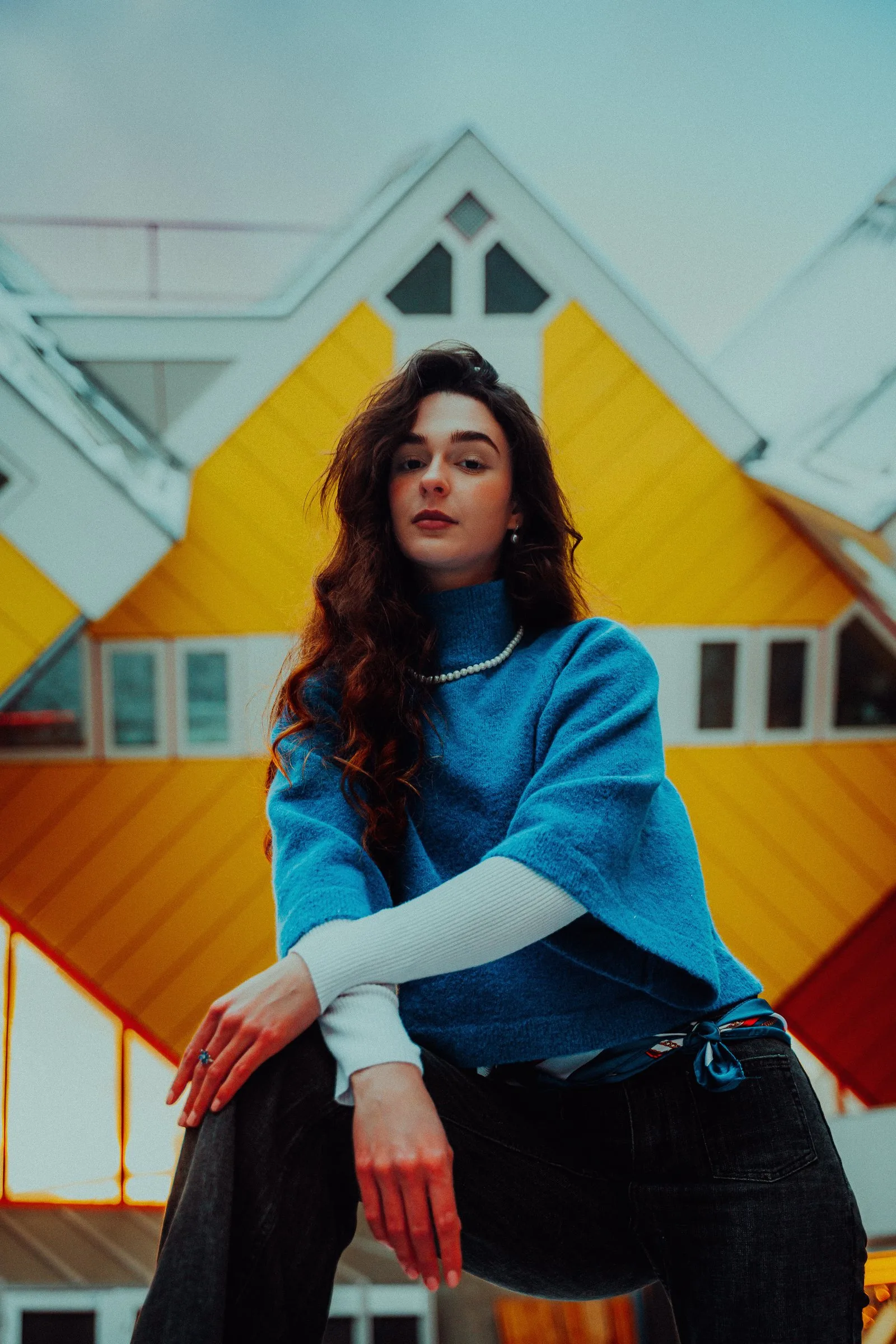 Femme en pull bleu devant des maisons cubiques jaunes