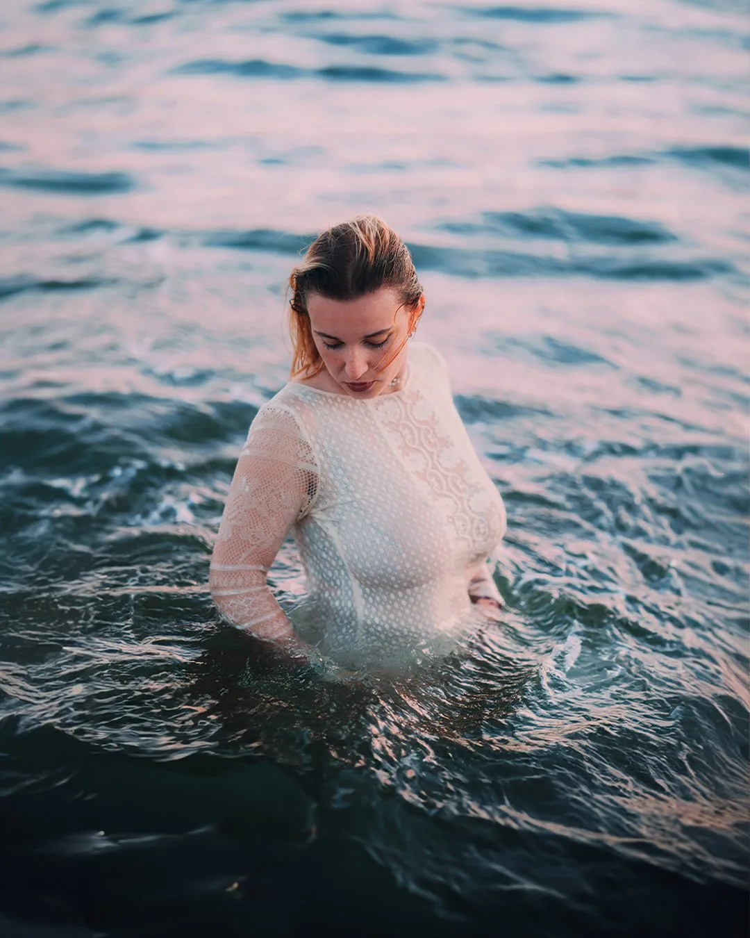 Jeune femme en pull blanc mouillé, dans la mer, le regard baissé vers l’eau