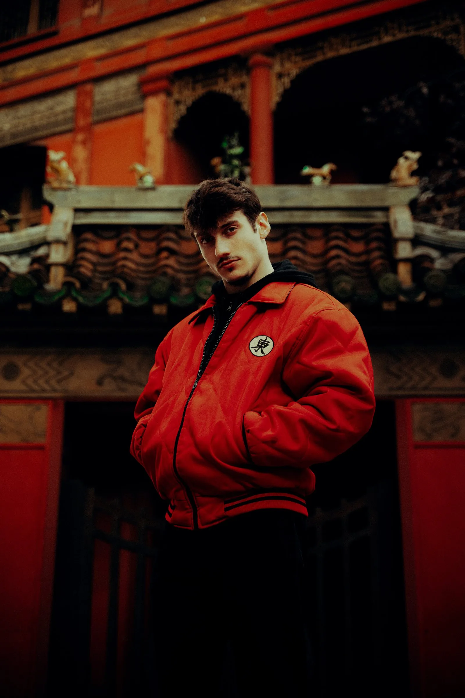 Jeune homme en blouson rouge devant une façade asiatique